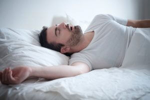 Man sleeping on bed with mouth open, showing signs of snoring or sleep apnea.