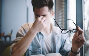 Man holding glasses and rubbing his eyes, showing signs of eye strain and fatigue.