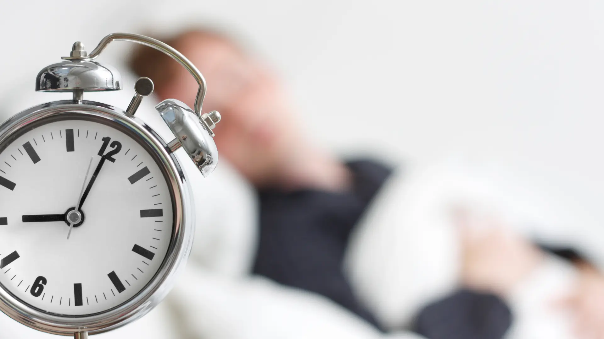 Blurred background of a person sleeping with an alarm clock in focus.