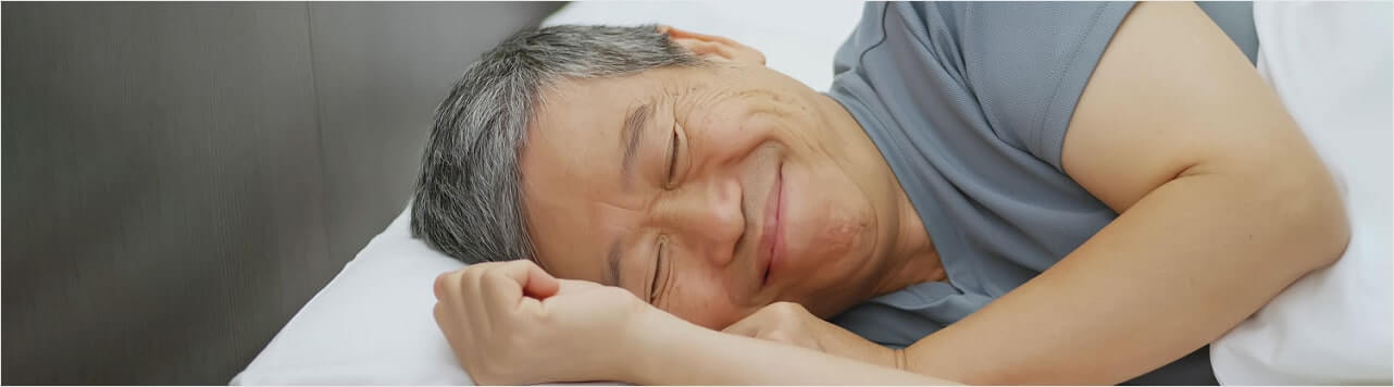 Older man smiling peacefully while sleeping in bed.