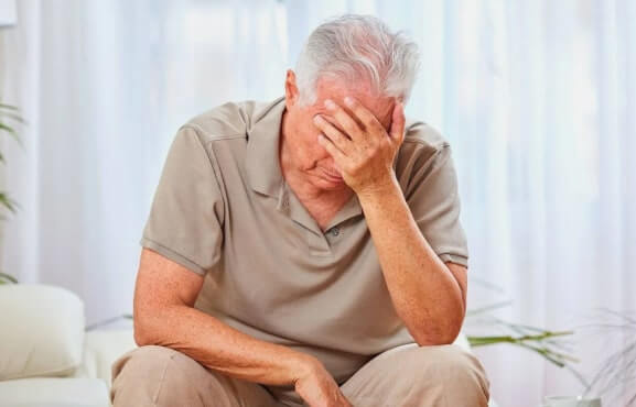 Senior man sitting with head in hand, showing fatigue or sleep-related exhaustion.