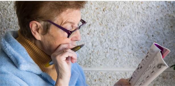 Senior woman wearing glasses concentrating on a puzzle book with pen in hand