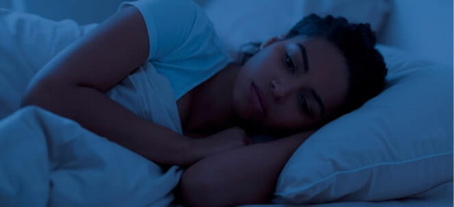 young woman lying awake in bed at night, looking thoughtful and unable to sleep
