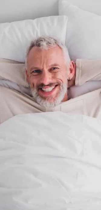 Smiling man with a gray beard lying in bed, looking well rested
