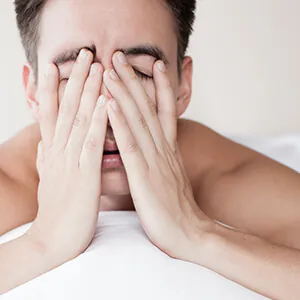 Tired man sitting in bed with hands covering his face, showing fatigue or sleep deprivation