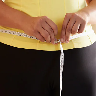 Person measuring their waist with a tape measure over workout clothes.