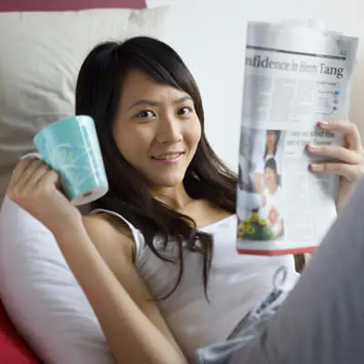 Young woman relaxing on a couch while holding a coffee mug and reading a newspaper