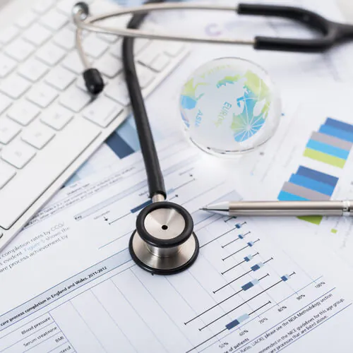 Stethoscope, charts, and graphs on a desk with a keyboard and pen, representing medical research and healthcare data analysis