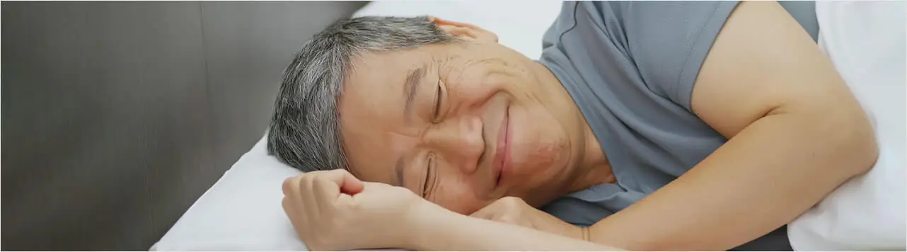 Older man smiling peacefully while sleeping in bed.