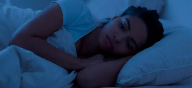 young woman lying awake in bed at night, looking thoughtful and unable to sleep